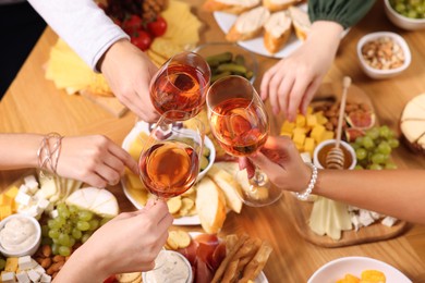 People clinking glasses with rose wine above wooden table, closeup