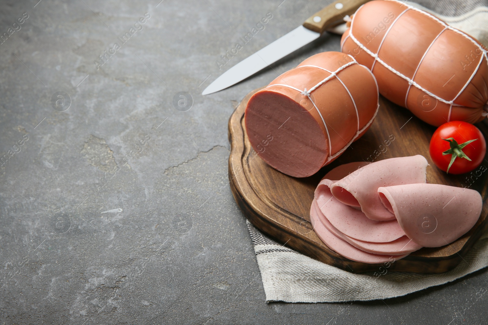 Photo of Board with tasty boiled sausages and tomato on grey textured table. Space for text