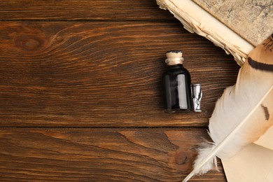 Photo of Feather pen, bottle of ink and old book on wooden table, flat lay. Space for text