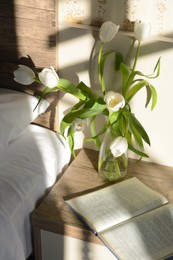 Beautiful white tulip bouquet and open book on nightstand in bedroom