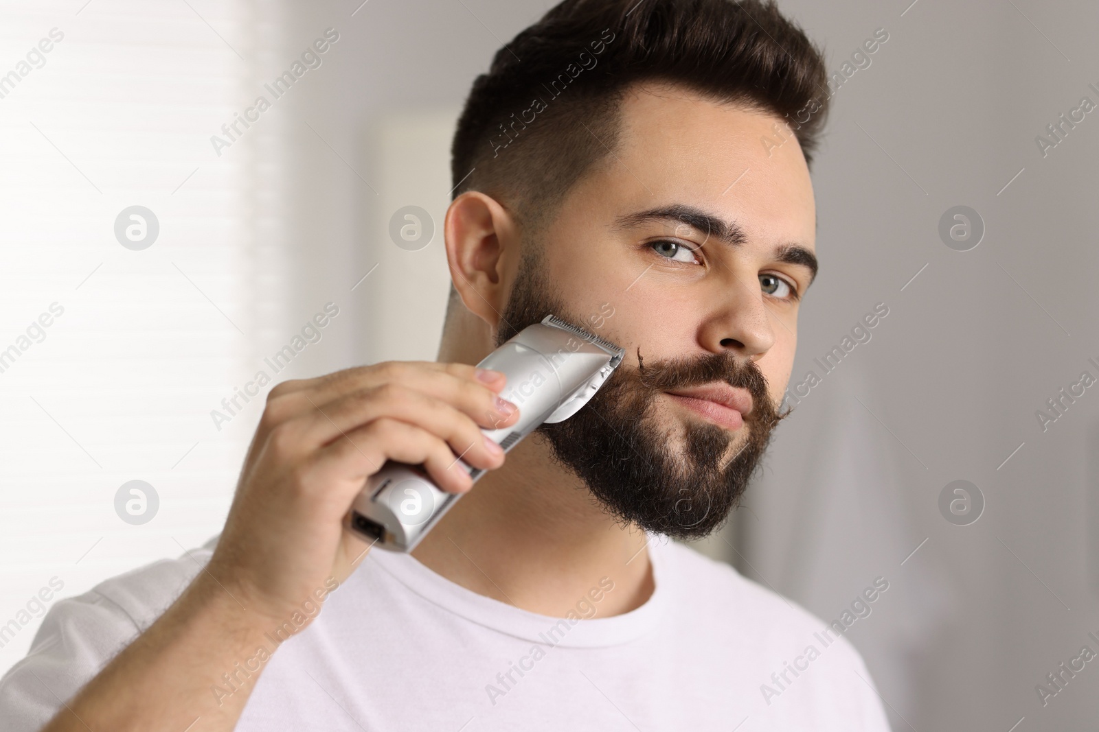 Photo of Handsome young man trimming beard at home