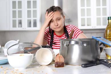 Photo of Upset woman in messy kitchen. Many dirty dishware and utensils on table, selective focus