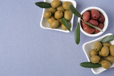 Different fresh olives and leaves on violet background, flat lay. Space for text