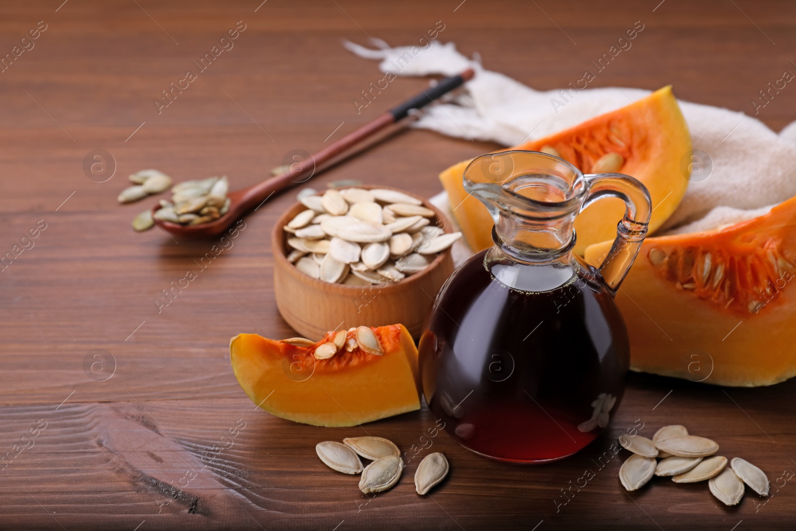 Photo of Fresh pumpkin seed oil in glass jug on wooden table. Space for text