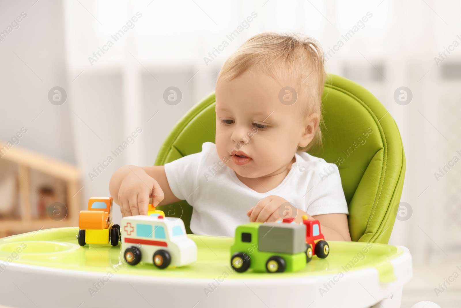 Photo of Children toys. Cute little boy playing with toy cars in high chair at home