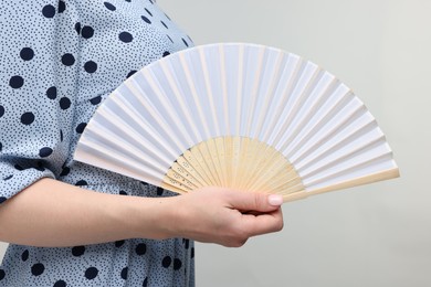Woman with hand fan on light grey background, closeup
