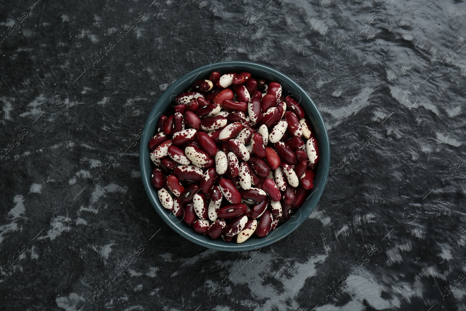 Photo of Bowl with dry kidney beans on black textured table, top view