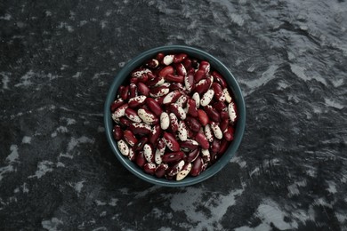 Bowl with dry kidney beans on black textured table, top view