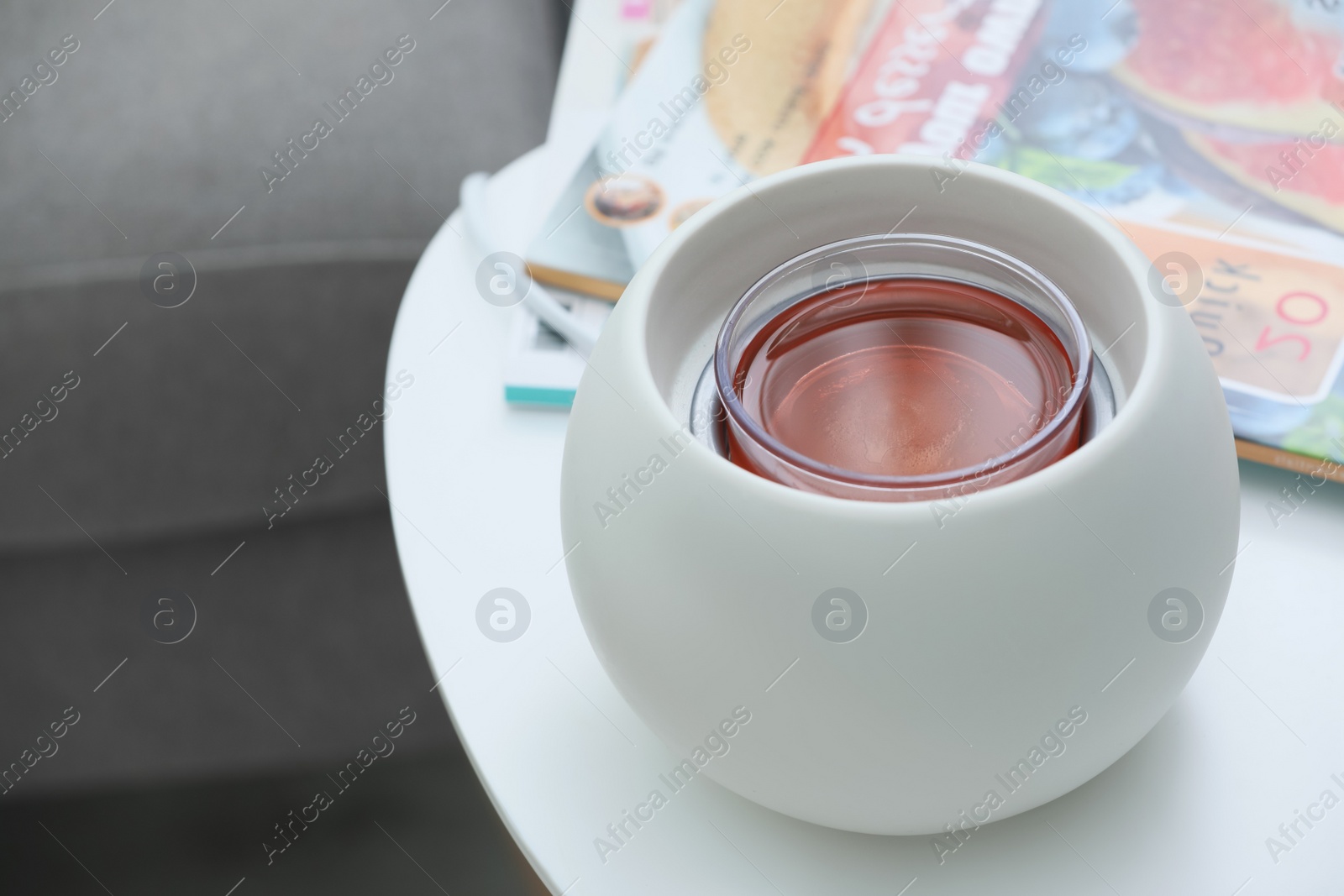 Photo of Wax air freshener and magazines on white table indoors. Interior elements