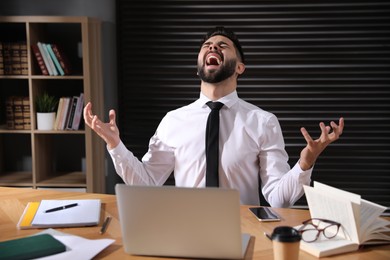 Photo of Emotional young businessman working on laptop in office. Online hate concept