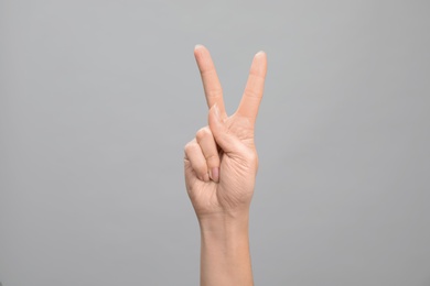 Photo of Woman showing number two on grey background, closeup. Sign language