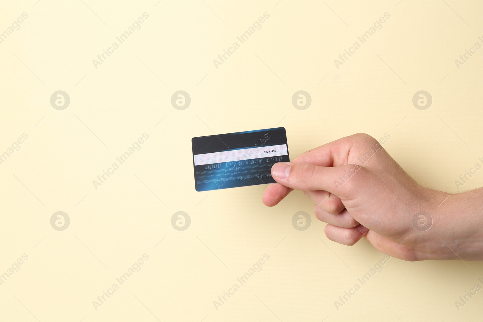 Photo of Man holding credit card on pale yellow background, closeup