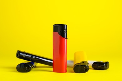 Stylish small pocket lighters on yellow background