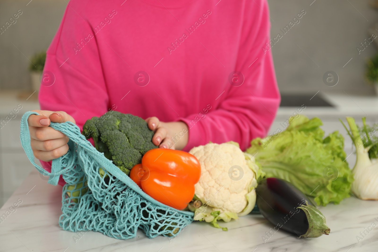 Photo of Woman with string bag of fresh vegetables at light marble table, closeup
