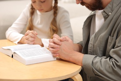 Girl and her godparent praying over Bible together at table indoors, closeup