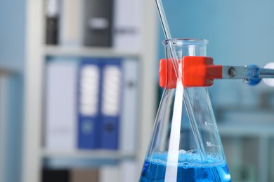 Photo of Laboratory analysis. Glass flask with blue liquid on stand indoors, closeup. Space for text