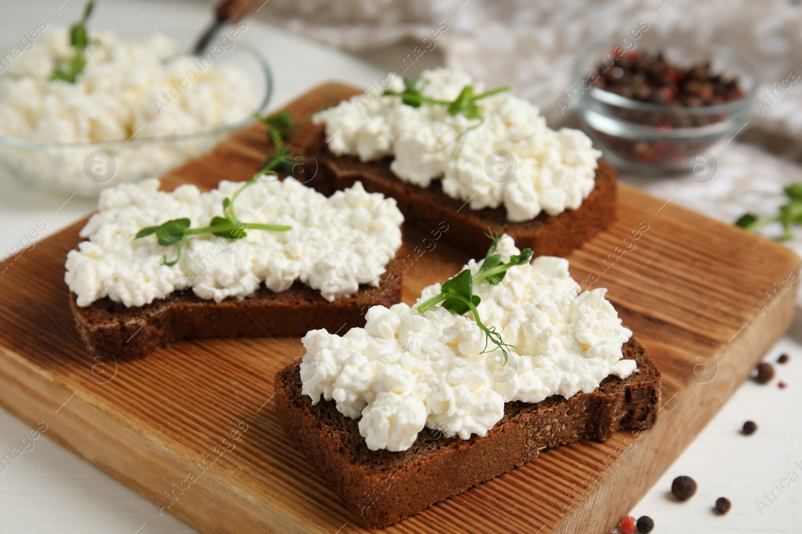 Photo of Bread with cottage cheese and microgreens on white table, closeup