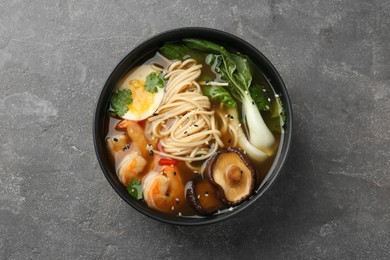 Photo of Delicious ramen with shrimps and egg in bowl on grey textured table, top view. Noodle soup