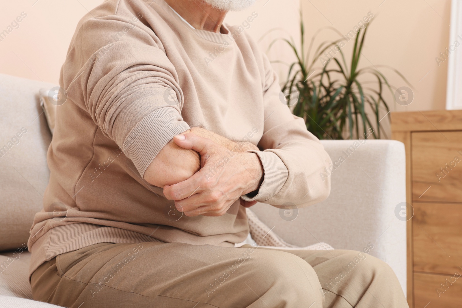 Photo of Senior man suffering from pain in his hand at home, closeup. Arthritis symptoms