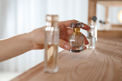 Photo of Woman taking bottle of perfume from wooden shelf indoors, closeup