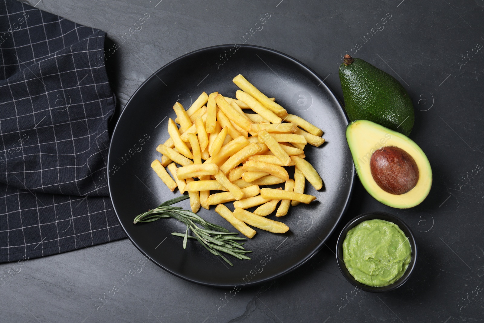 Photo of Plate with french fries, guacamole dip, rosemary and avocado served on black table, flat lay