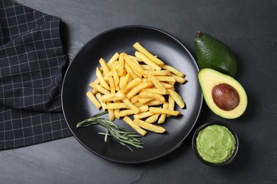 Photo of Plate with french fries, guacamole dip, rosemary and avocado served on black table, flat lay