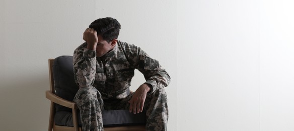 Photo of Stressed military officer sitting in armchair near white wall indoors. Space for text