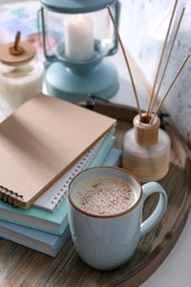 Wooden tray with books, air reed freshener and cup of coffee on white table indoors