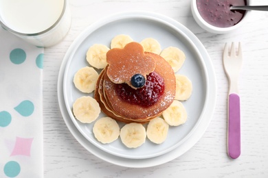 Photo of Tasty pancakes served with jam and milk on white wooden table, flat lay. Creative idea for kids breakfast