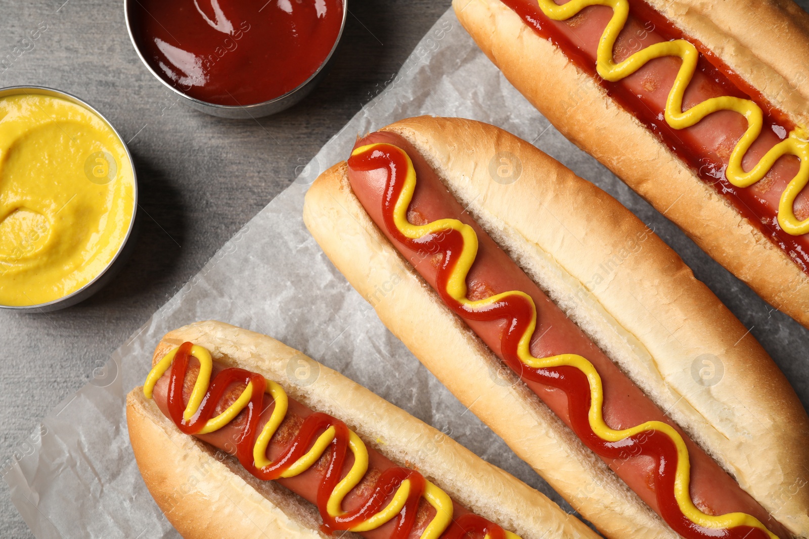 Photo of Delicious hot dogs with mustard and ketchup on grey table, flat lay