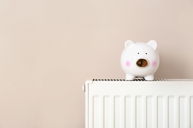 Photo of Piggy bank on heating radiator against light background. Space for text