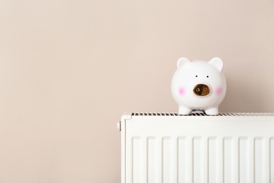 Piggy bank on heating radiator against light background. Space for text