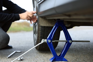 Man changing car tire, focus on scissor jack outdoors