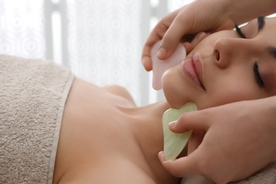 Young woman receiving facial massage with gua sha tools in beauty salon, closeup