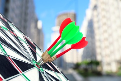 Board with color darts hitting target against blurred view of cityscape