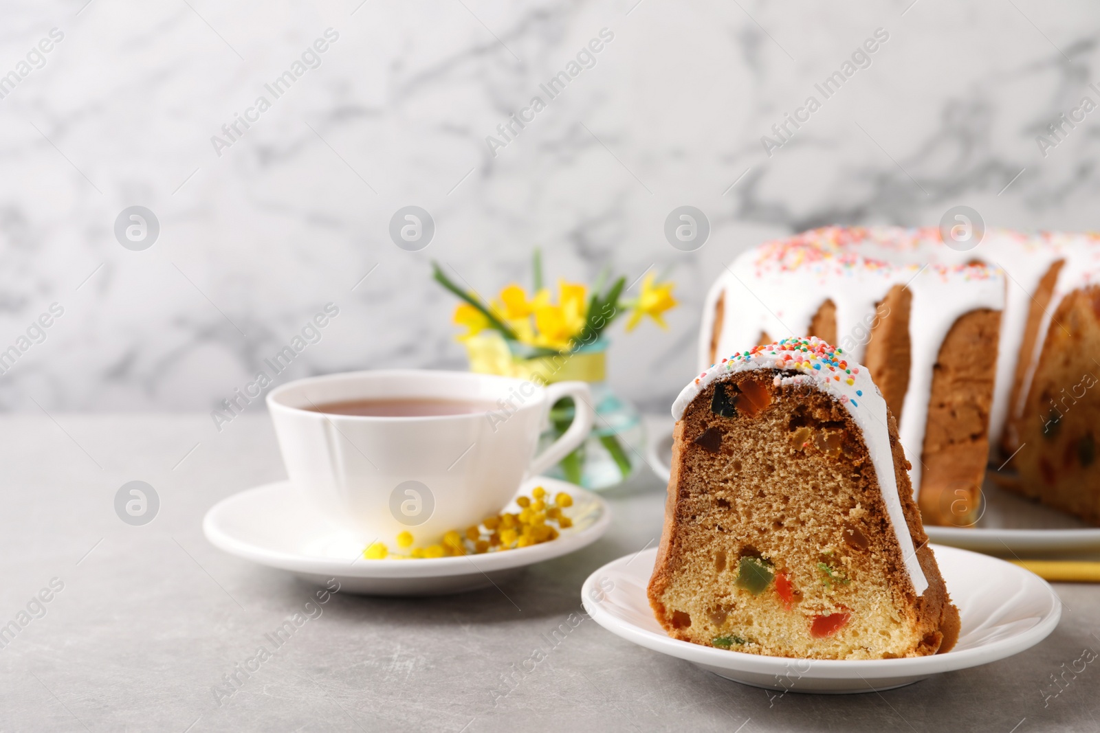 Photo of Piece of glazed Easter cake with sprinkles and tea on grey table, space for text