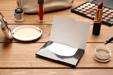 Facial oil blotting tissues and different decorative cosmetics on wooden table. Mattifying wipes