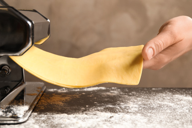 Woman preparing dough with pasta maker machine at table, closeup