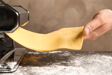 Photo of Woman preparing dough with pasta maker machine at table, closeup