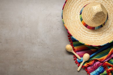 Photo of Mexican sombrero hat, maracas and colorful poncho on grey textured background, flat lay. Space for text