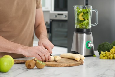 Photo of Man cutting bananas for delicious smoothie at white marble table in kitchen, closeup. Space for text