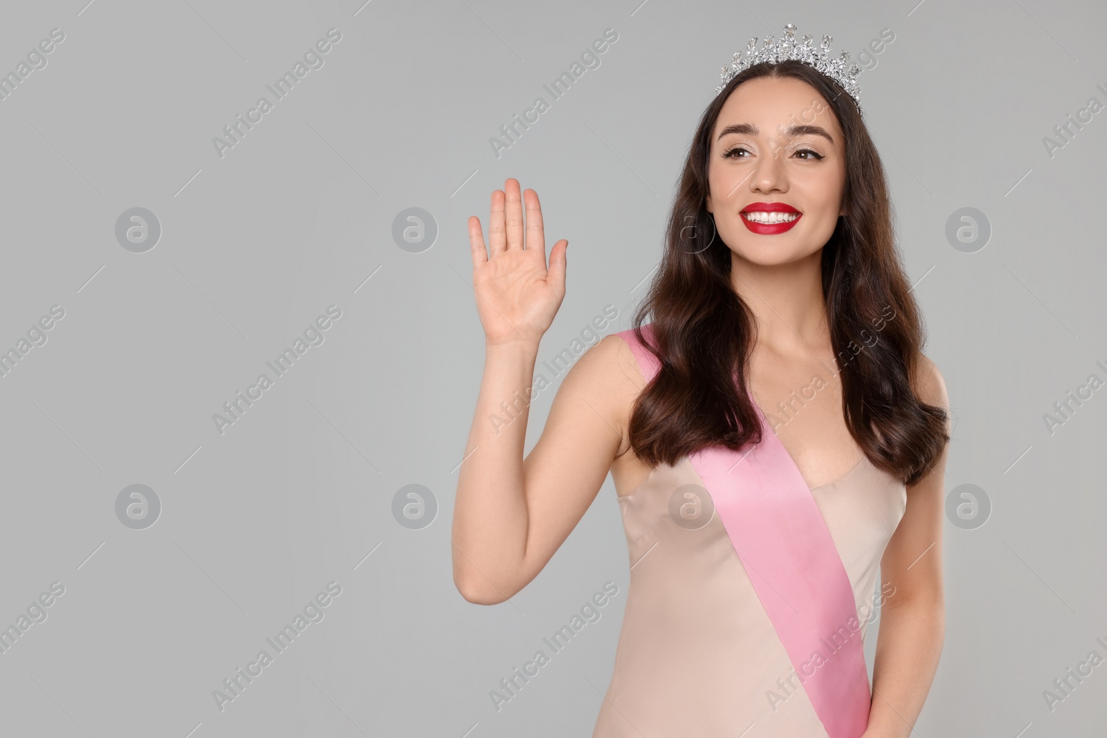 Photo of Beautiful young woman with tiara and ribbon in dress on grey background, space for text. Beauty contest