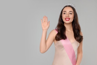 Photo of Beautiful young woman with tiara and ribbon in dress on grey background, space for text. Beauty contest