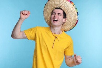 Young man in Mexican sombrero hat dancing on light blue background