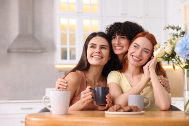 Photo of Happy young friends spending time together at table in kitchen