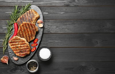 Delicious grilled pork steaks with spices on dark wooden table, flat lay. Space for text