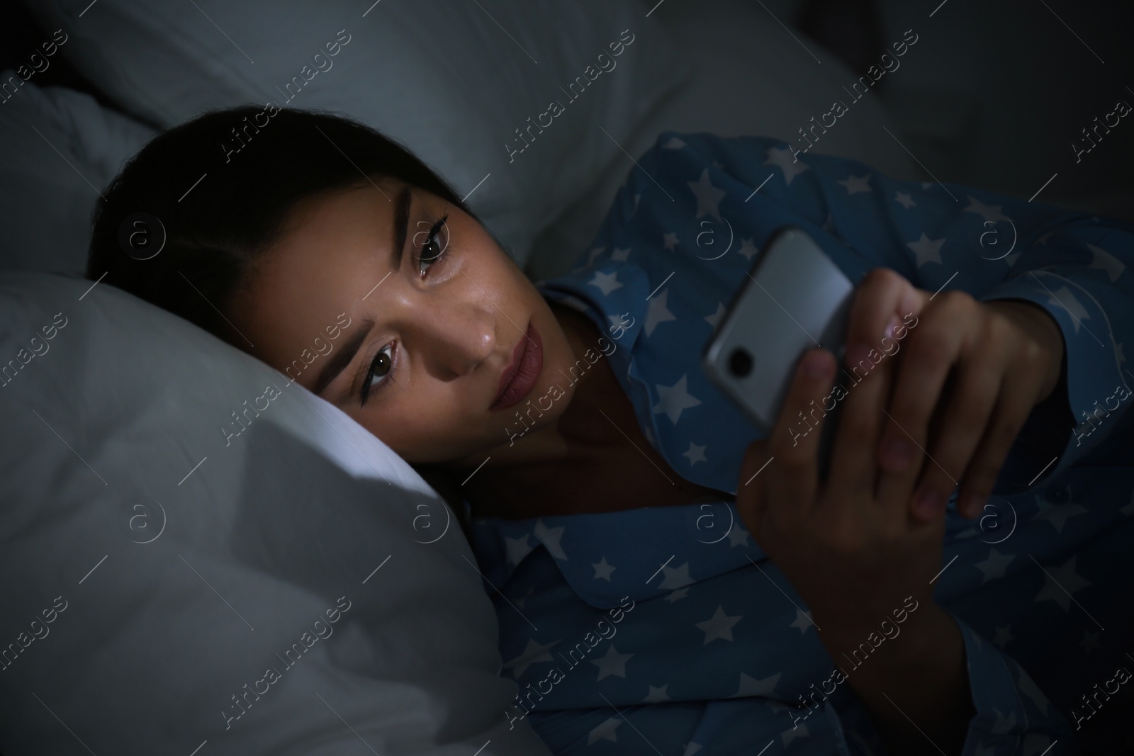 Photo of Young woman using mobile phone in dark bedroom