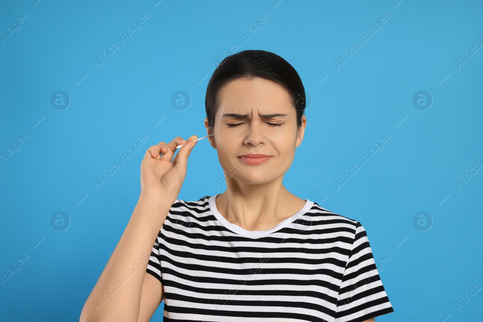 Photo of Young woman cleaning ear with cotton swab on light blue background