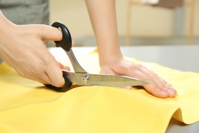 Seamstress cutting yellow fabric with scissors at workplace, closeup