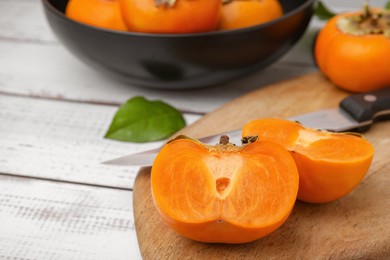 Photo of Whole and cut delicious ripe persimmons on white wooden table